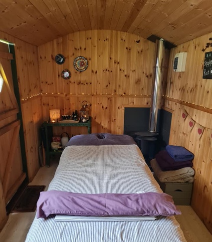 Photograph of inside shepherds rest hut showcasing the massage bed and log burner