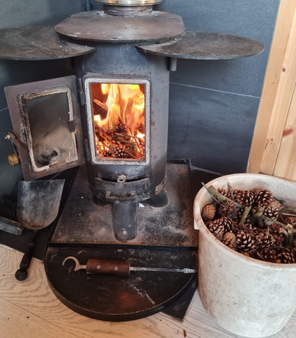 Photograph of the log burner inside of shepherds rest hut next to a container of pinecones